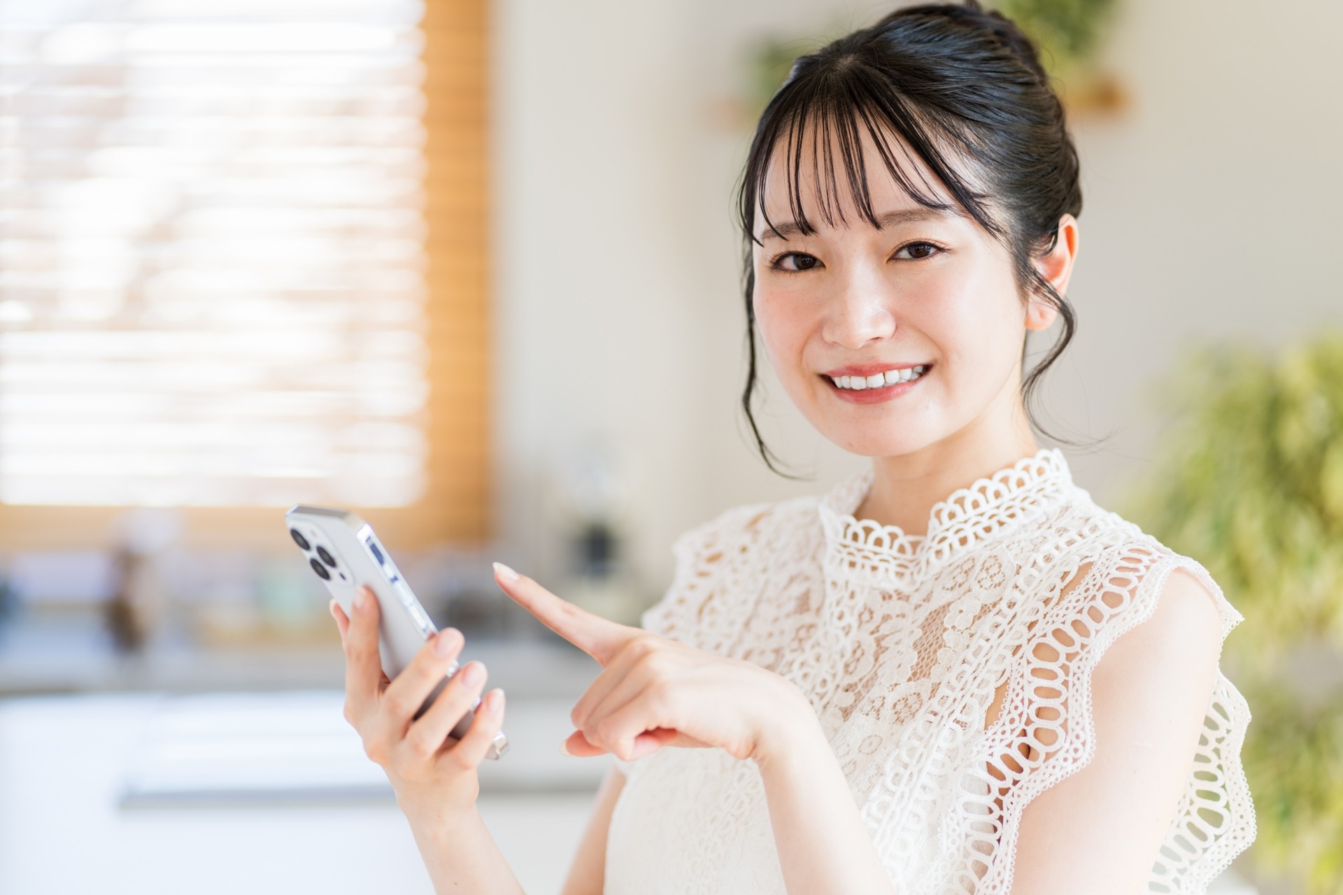 明るい自宅でスマートフォンを使う女性のイメージ